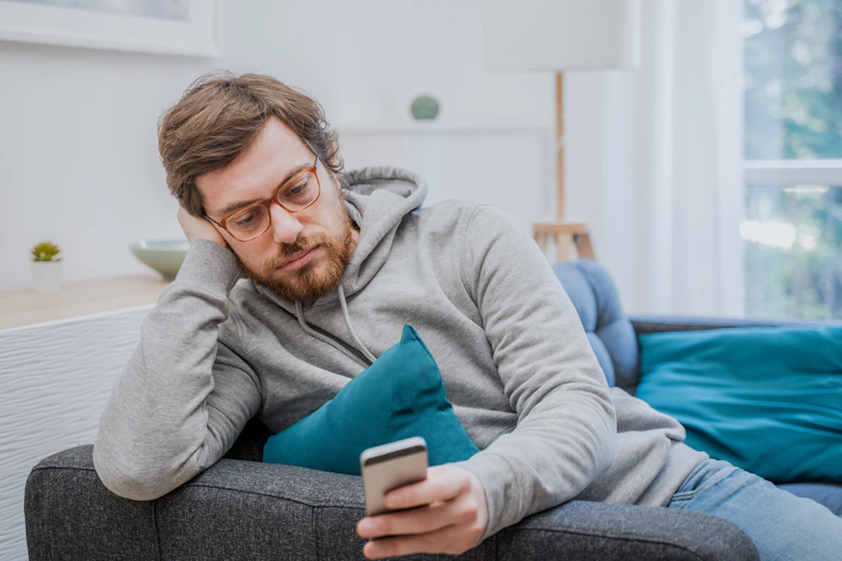 A young man in a grey hoodie looks at his phone.