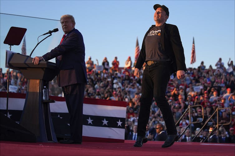 Two men standing on stage in front of a crowd of people.