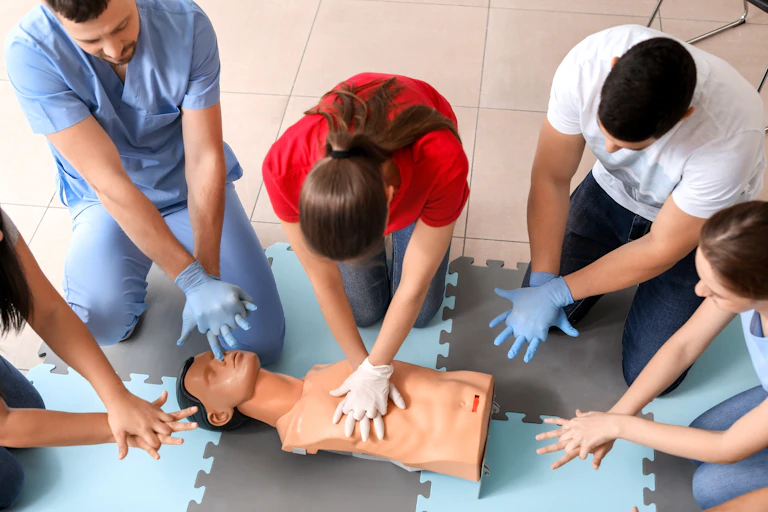 Medical staff crowd wearing gloves around a mannequin torso while one presses on its chest.