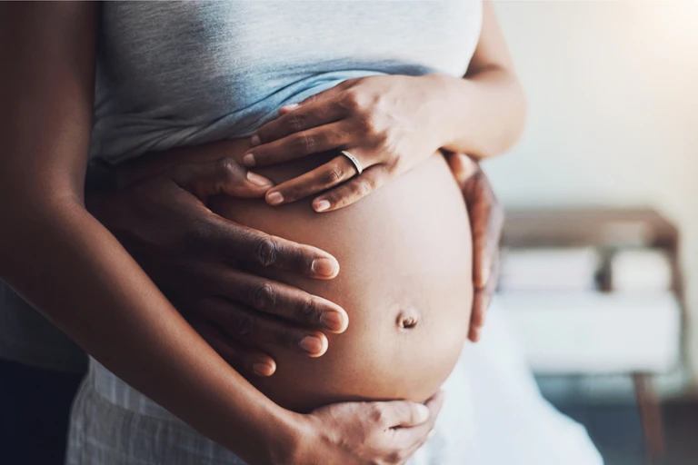 Black woman pregnant, hands on belly, partner behind her, hands on belly