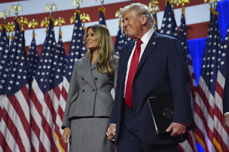 Donald and Melania Trump standing in front of US flags