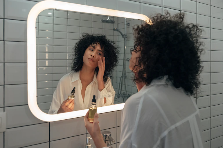 A woman applies a serum to her cheek.
