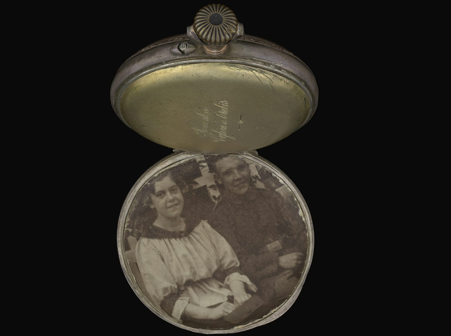 An open pocket watch showing a black-and-white photograph of a young German couple.