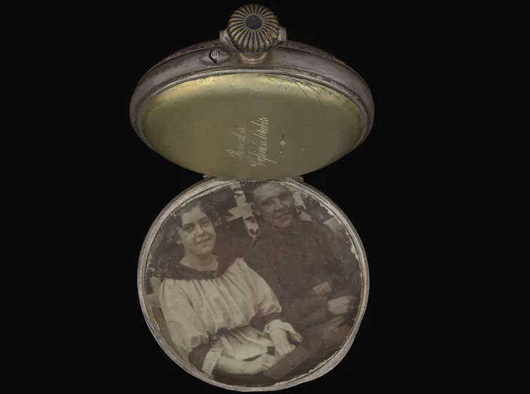 An open pocket watch showing a black-and-white photograph of a young German couple.