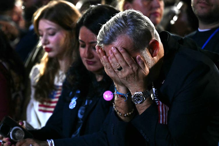 Three people look downcast and one man covers his face with his hands