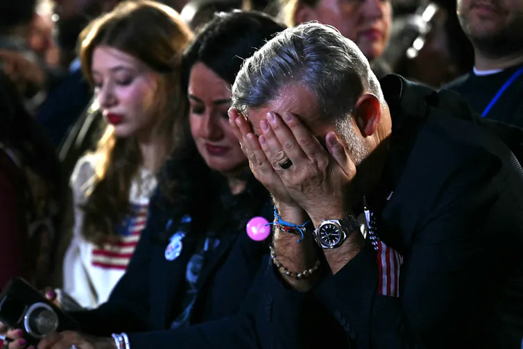 Three people look downcast and one man covers his face with his hands