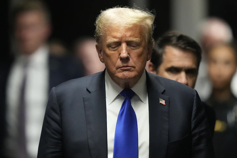 A man in a suit and tie stands with his eyes closed.