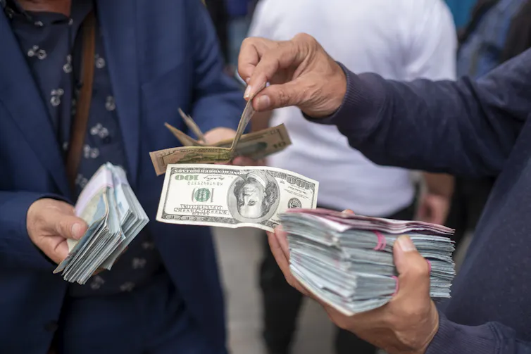 A man holds a hundred dollar bill while exchanging some more notes with another person.
