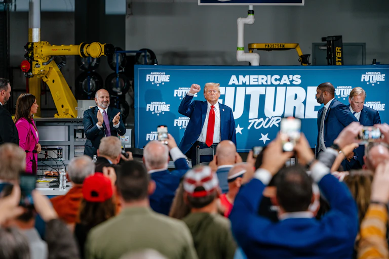 US Republican presidential candidate Donald J. Trump raises his fist for a crowd in a factory, in front of a banner that reads America's Future Tour