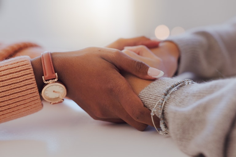 A woman's hands hold another woman's hands.