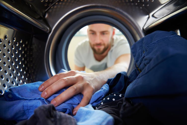 View from inside the washing machine with a man reaching out pulling out clean laundry.