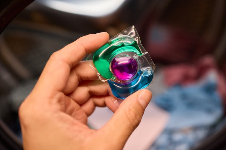 A colourful green, blue and purple plastic sachet about to be placed in a washing machine.