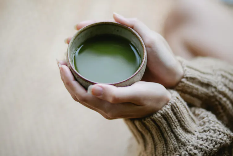 Mãos segurando uma xícara de matcha.