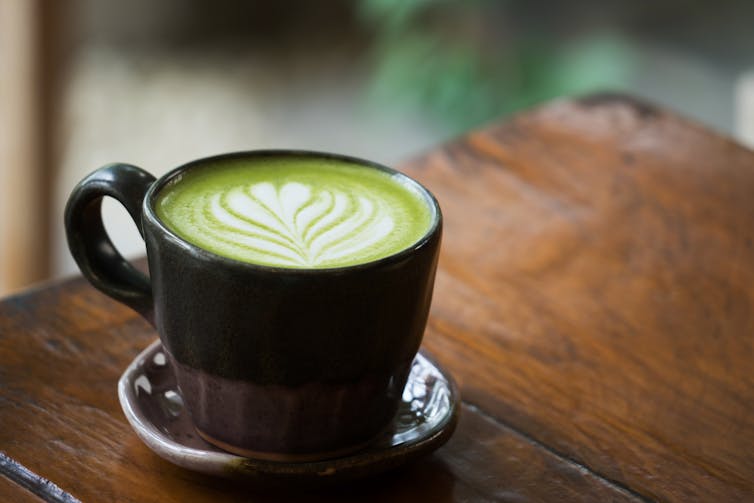 A matcha latte in a black cup on a brown table.