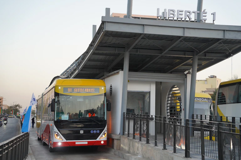 A red and yellow electric bus parked under a smart new bus shelter