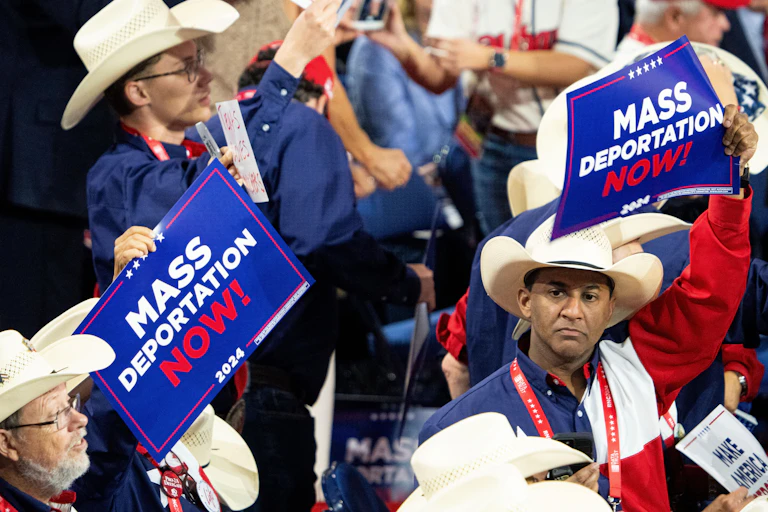 Men in cowboy hats in a crowd holding 'Mass deportation now' signs.