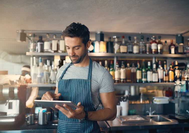 bar owner standing in front of his bar looking at a tablet