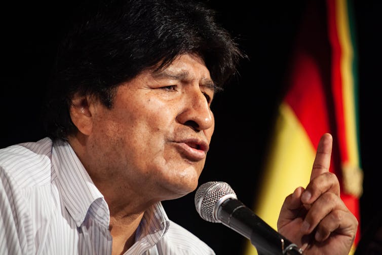 Evo Morales speaking into a microphone with his finger pointing towards the sky.