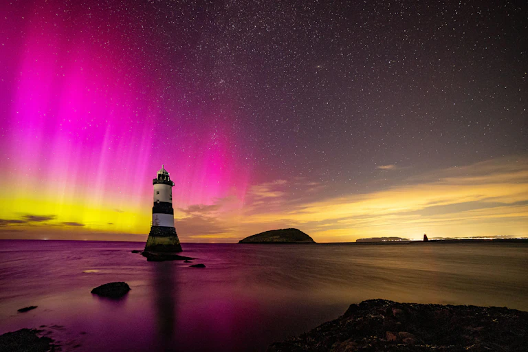 The aurora borealis over a black and white lighthouse.