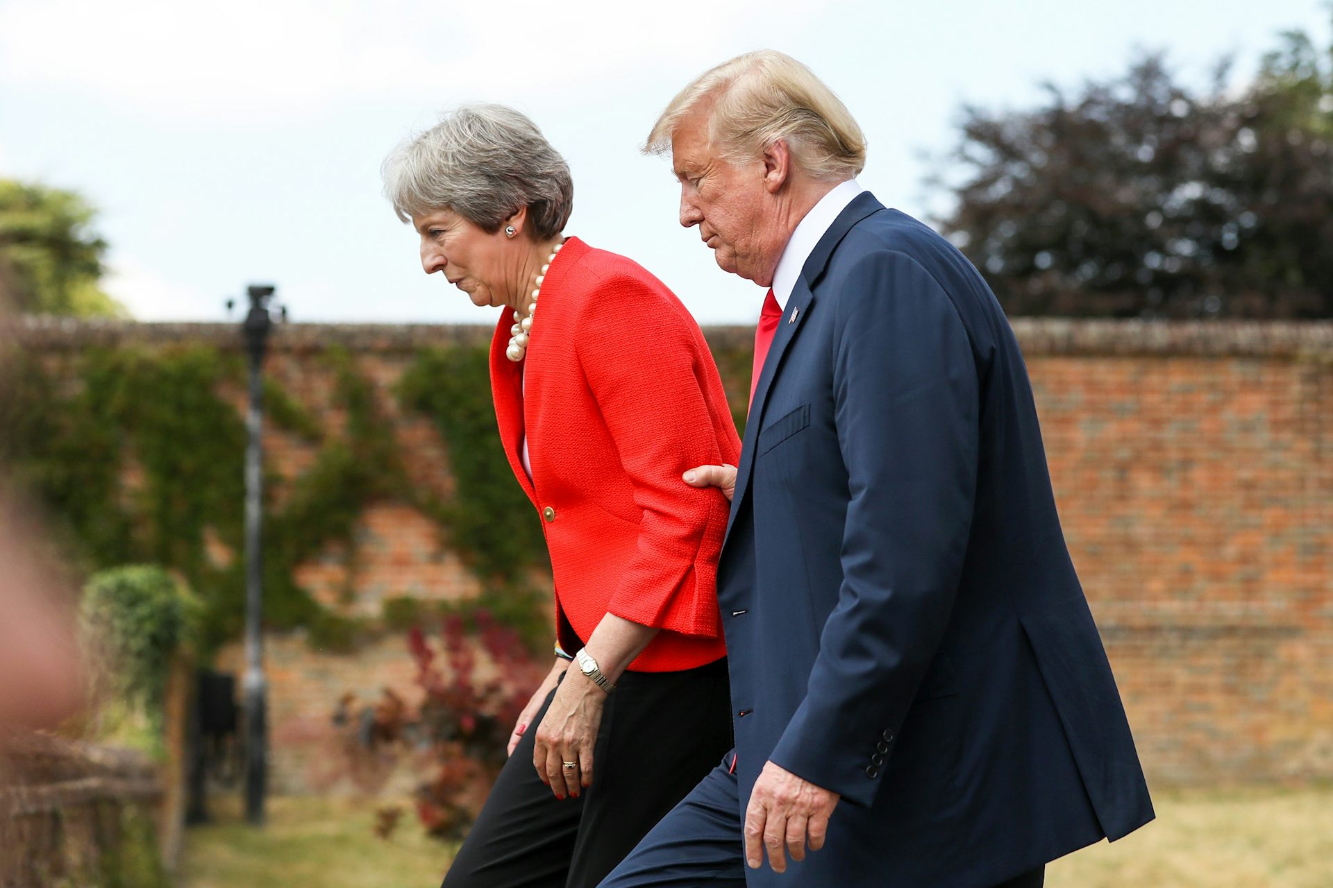 Side view of Trump and Theresa May walking side-by-side, with Trump grabbing firmly on to May's elbow.