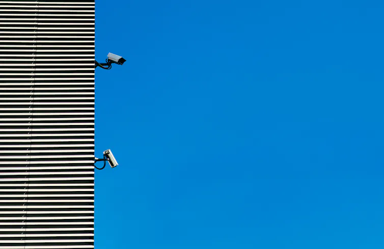 Two surveillance cameras on the side of a building against a blue sky.