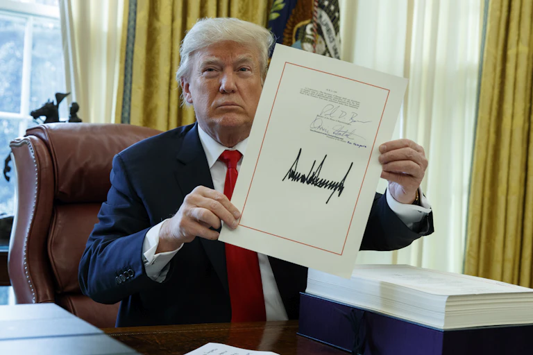 a man in a suit sitting at a desk holds up a document with his signature