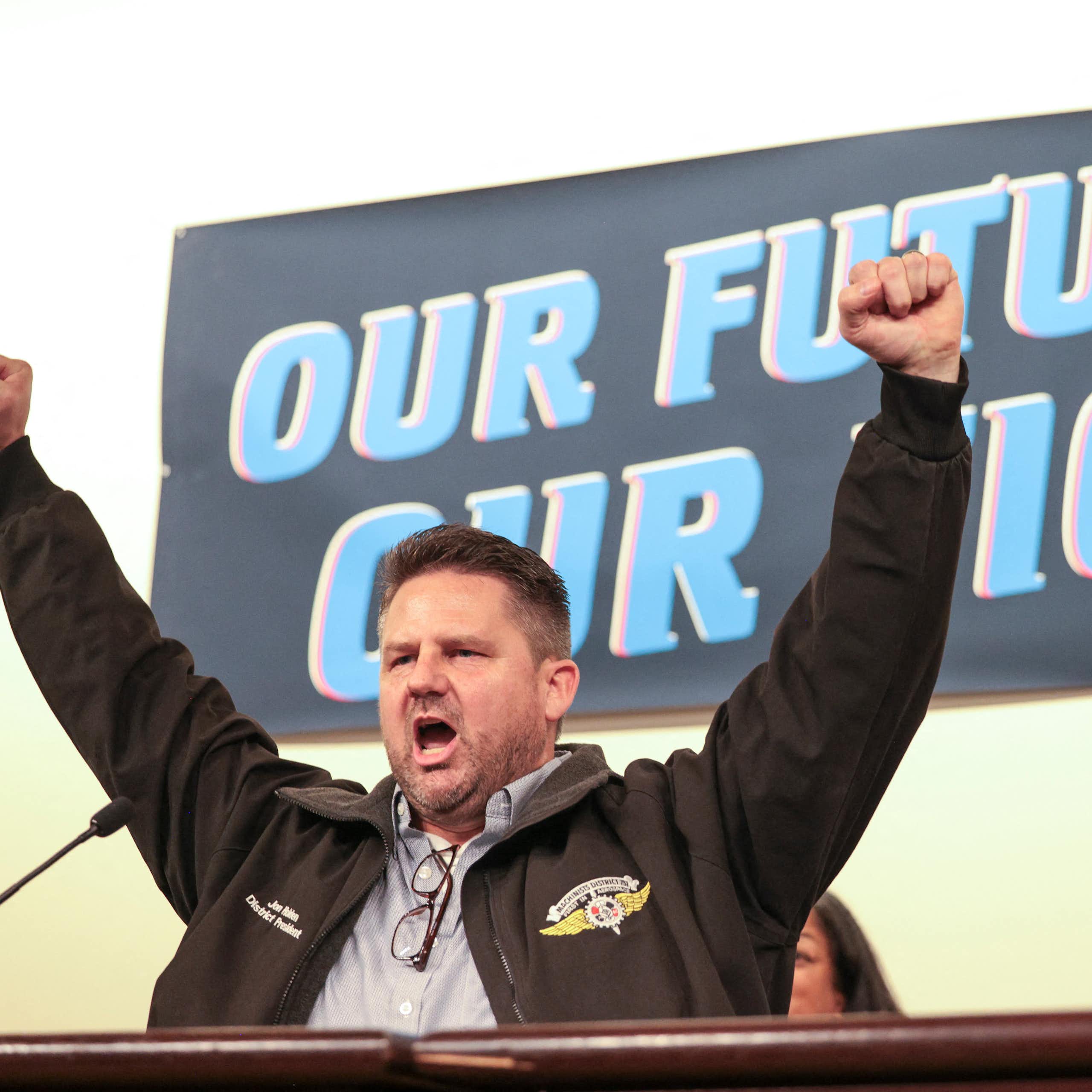 A man holds his arms aloft, hands balled into fists, against a banner that says 'our future our fight.'