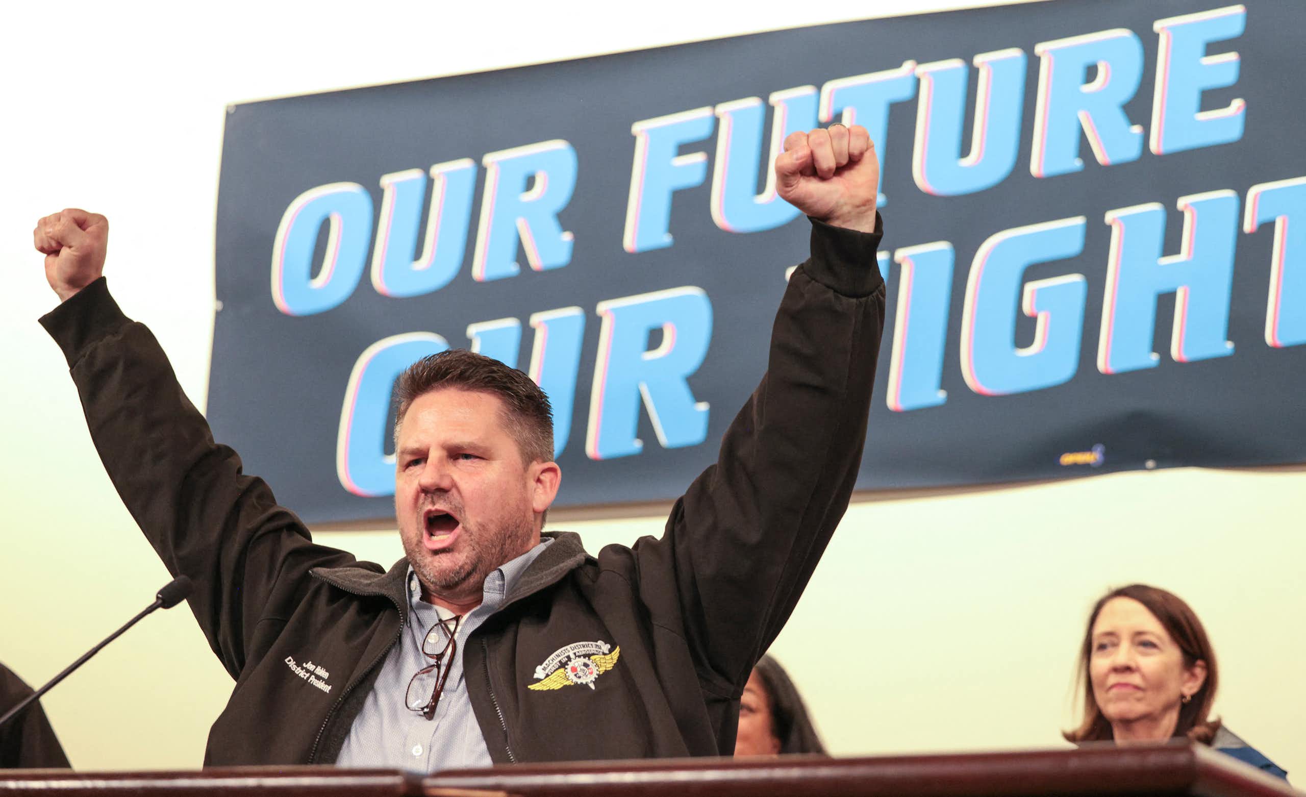 A man holds his arms aloft, hands balled into fists, against a banner that says 'our future our fight.'