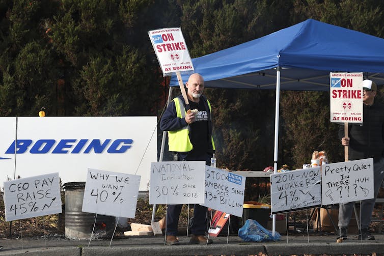 A Boeing worker walks among signs that say why he's on strike.