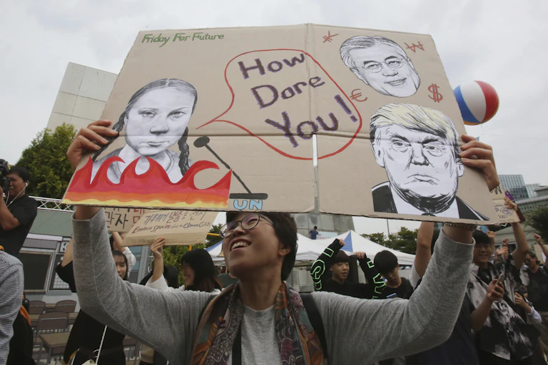 woman holds sign with three faces and the words 'how dare you?'