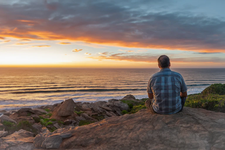 A man sitting on a rock looking out to sea.