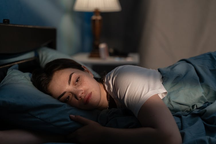 A woman lying in bed in the dark.