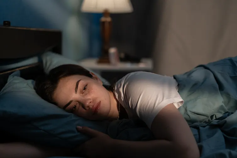 A woman lying in bed in the dark.
