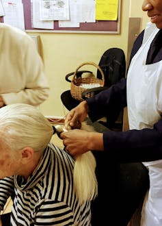 An elderly woman's hair is tied up by an African woman caregiver.