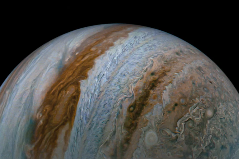 Uma imagem de Júpiter mostra o topo das nuvens e os cinturões coloridos azuis e marrons que cobrem o planeta.