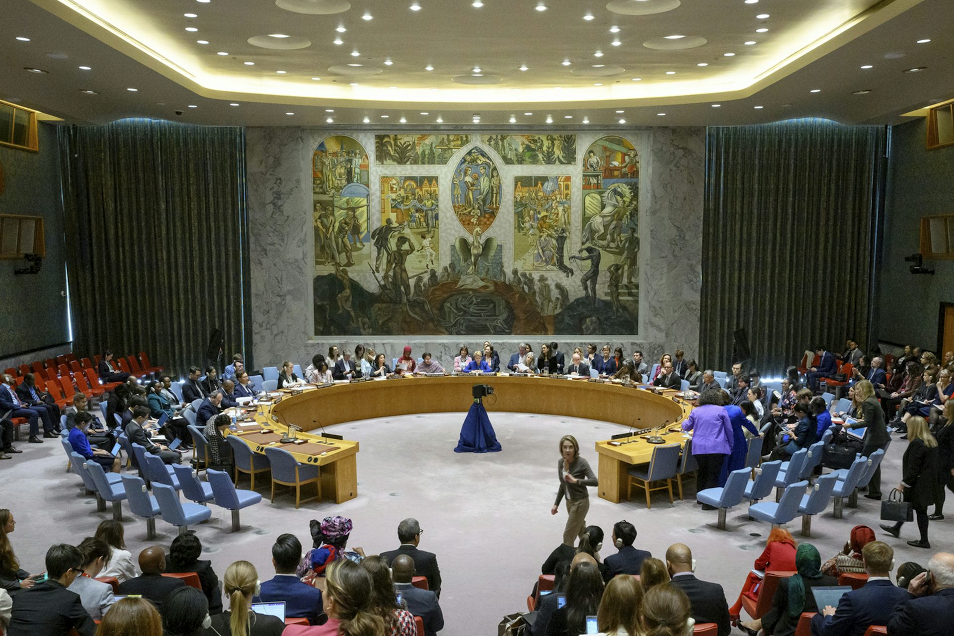 A ornate meeting room with several people seated around an arc-shaped table.