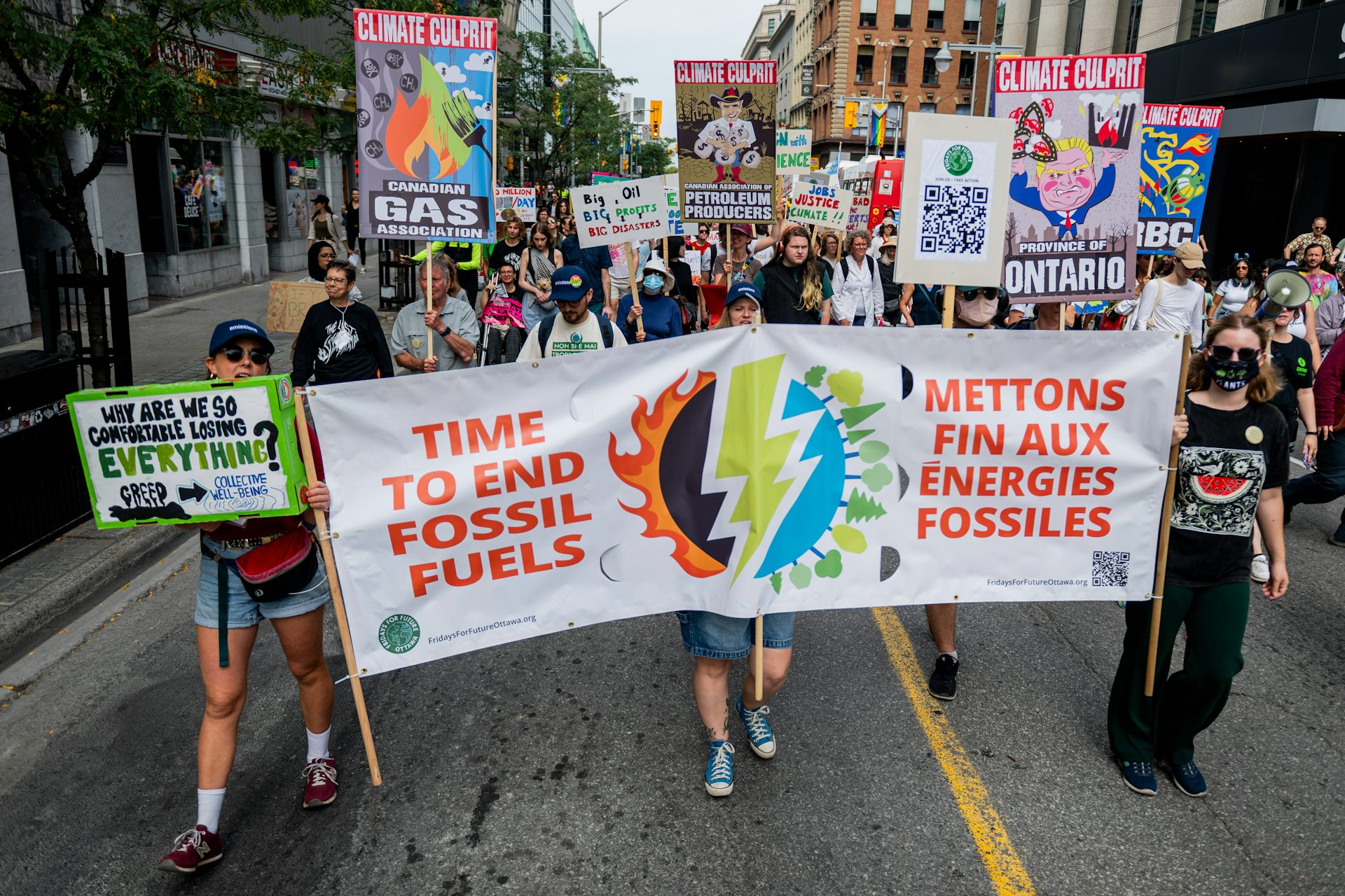 A group of protesters walk through a city street holding banners and signs.
