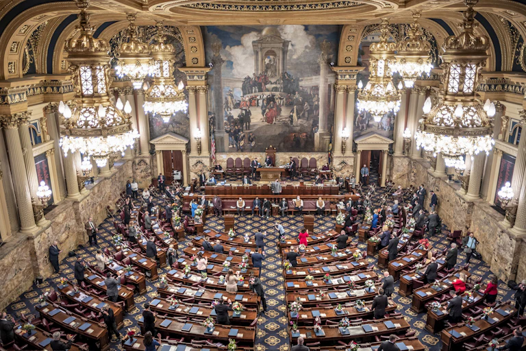 Aerial view of grand room with chandeliers, oil paintings and dozesn of people seated and standing at long wooden tables