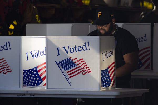 Man with beard and wearing black Pittsburgh Pirates ballcap casts ballot behind screen that says 'I Voted!'