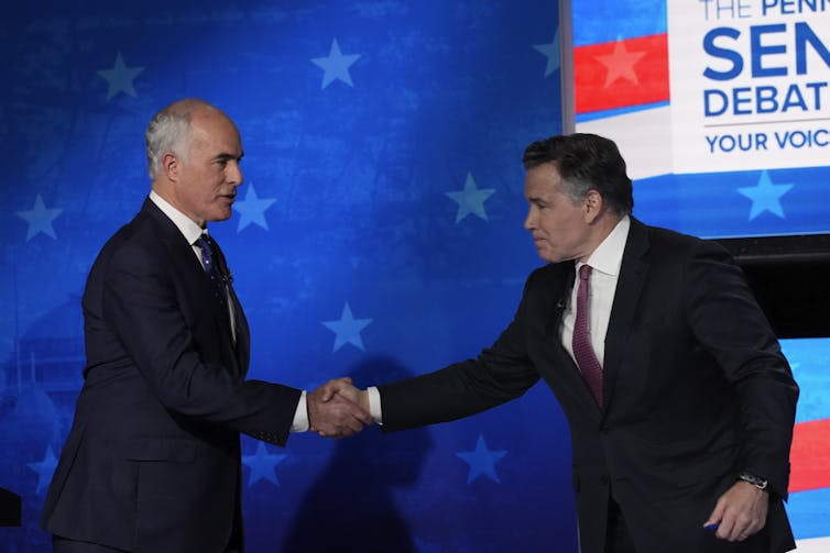 Two men in dark suits shake hands on a debate stage