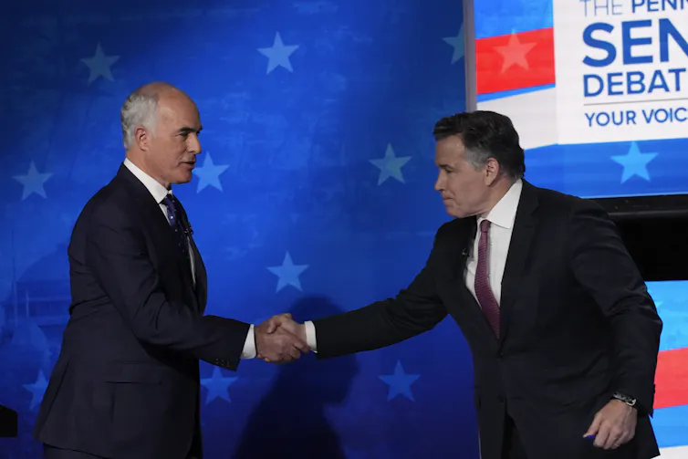 Two men in dark suits shake hands on a debate stage