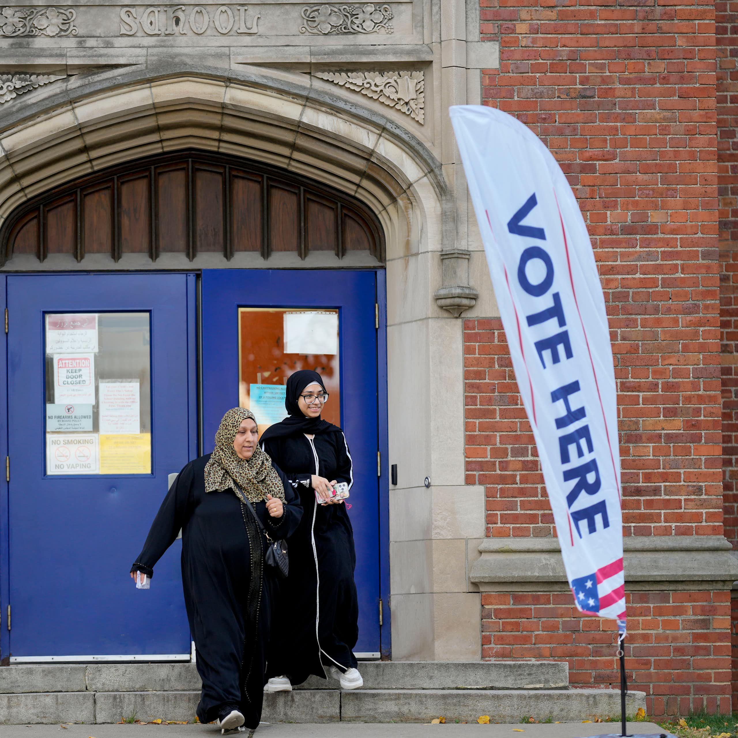 Two woman wearing head scarves and modest clothing smile as they exit a polling place