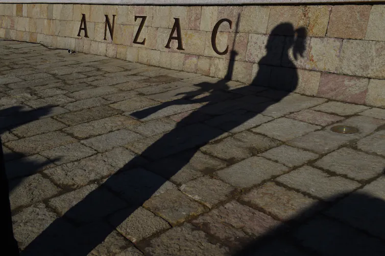 A woman's silhouette is seen against the word ANZAC displayed on a sign.