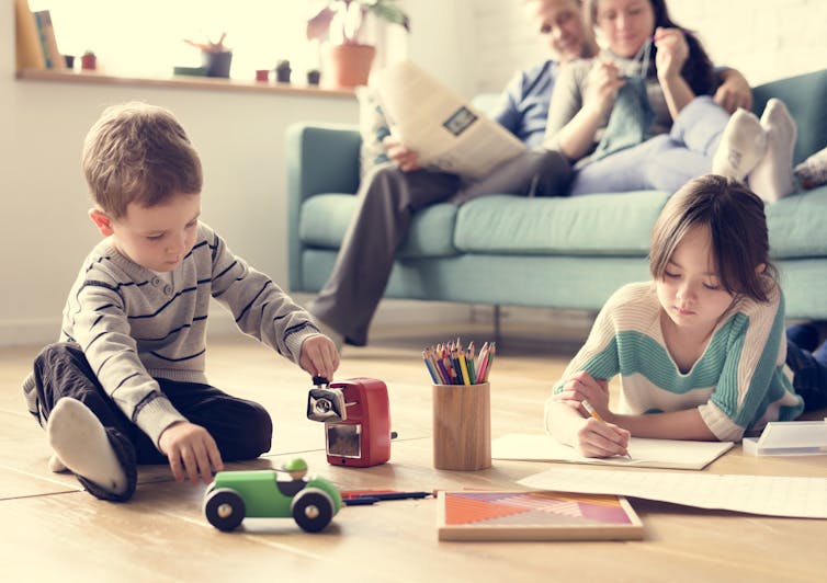 kids (boy & girl) playing on floor in front of sofa (with relexed parents)