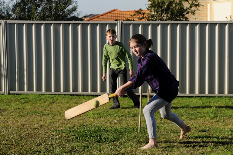 A young boy and girl play backyard cricket