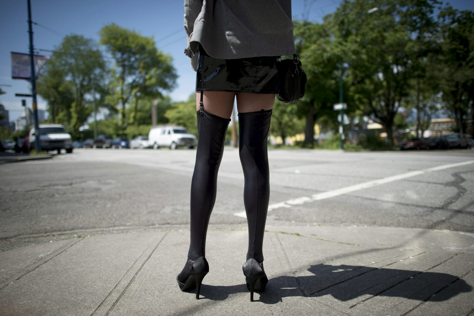 Closeup of a woman wearing black heeled shoes and leggings standing on the corner of an intersection.