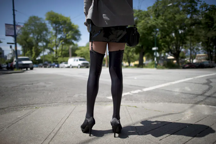 Closeup of a woman wearing black heeled shoes and leggings standing on the corner of an intersection.
