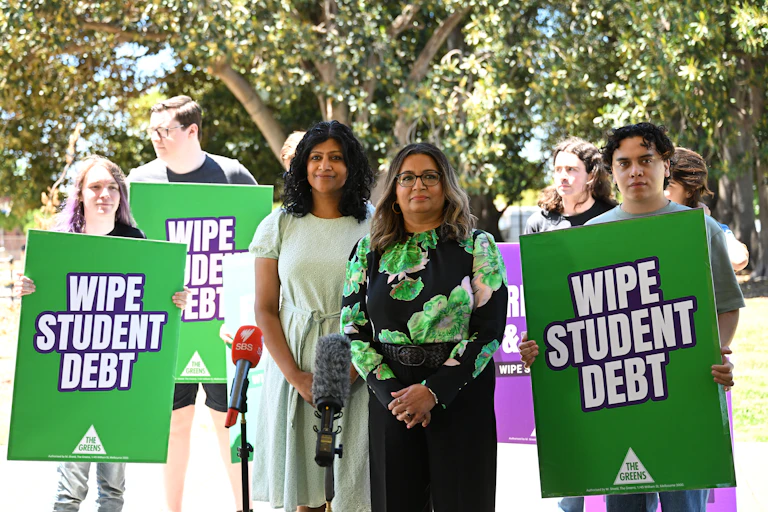 Greens education spokesperson Mehreen Faruqi at a media conference. Supporters hold 'wipe student debt' signs.