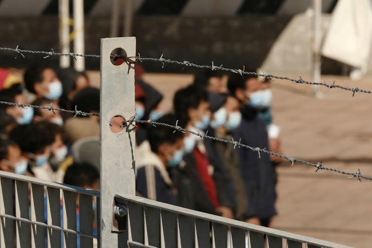 Photo showing a group of people out of focus, behind a barbed wire fence