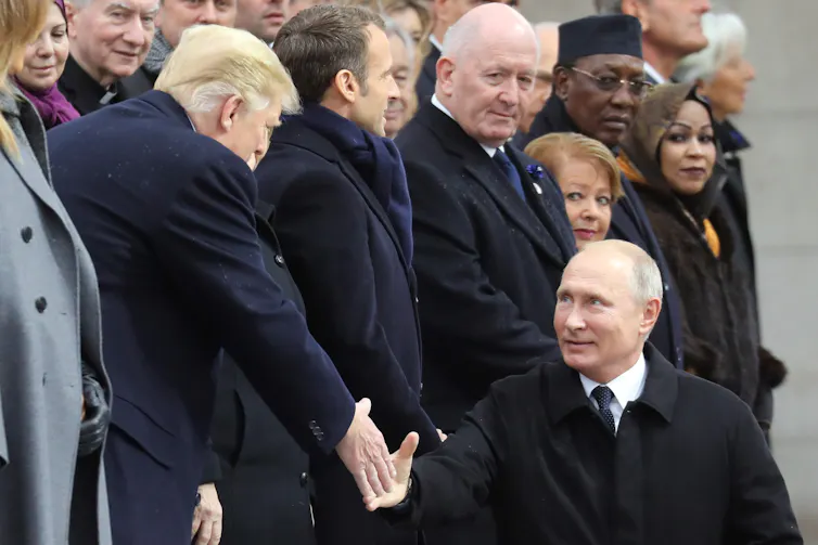Donald Trump and Vladimir Putin shake hands surrounded by other world leaders.